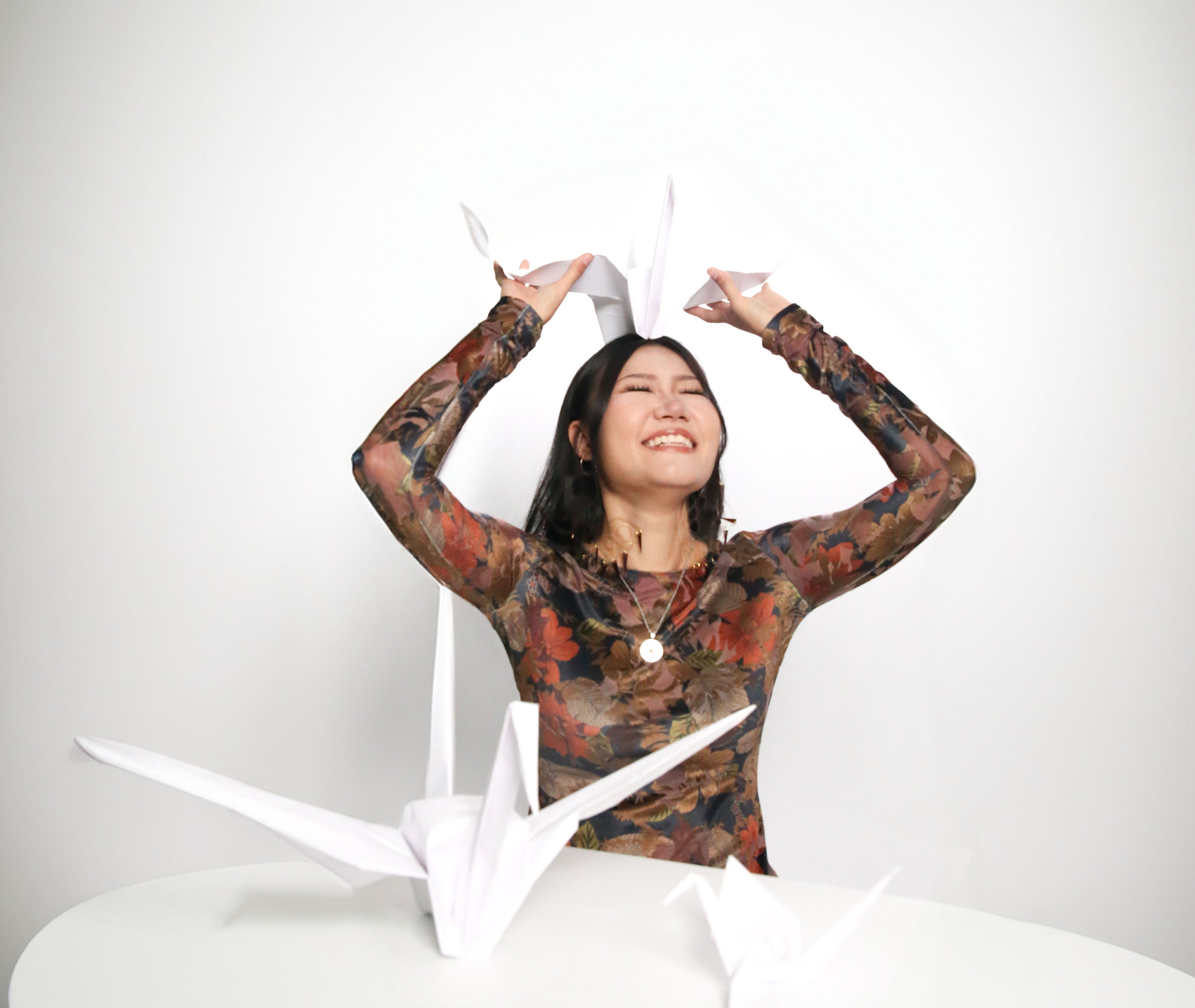 model  is smiling wearing soft velvet long sleeve top with autumn floral burn out fabric. model is holding origami cranes.